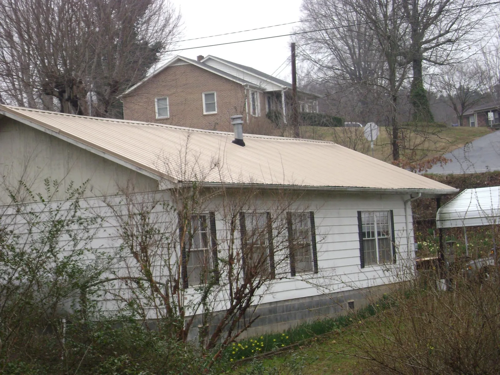 Tan metal roof on a white sided house set into a hillside — Commercial Roofing by Roofing Brothers in Peoria